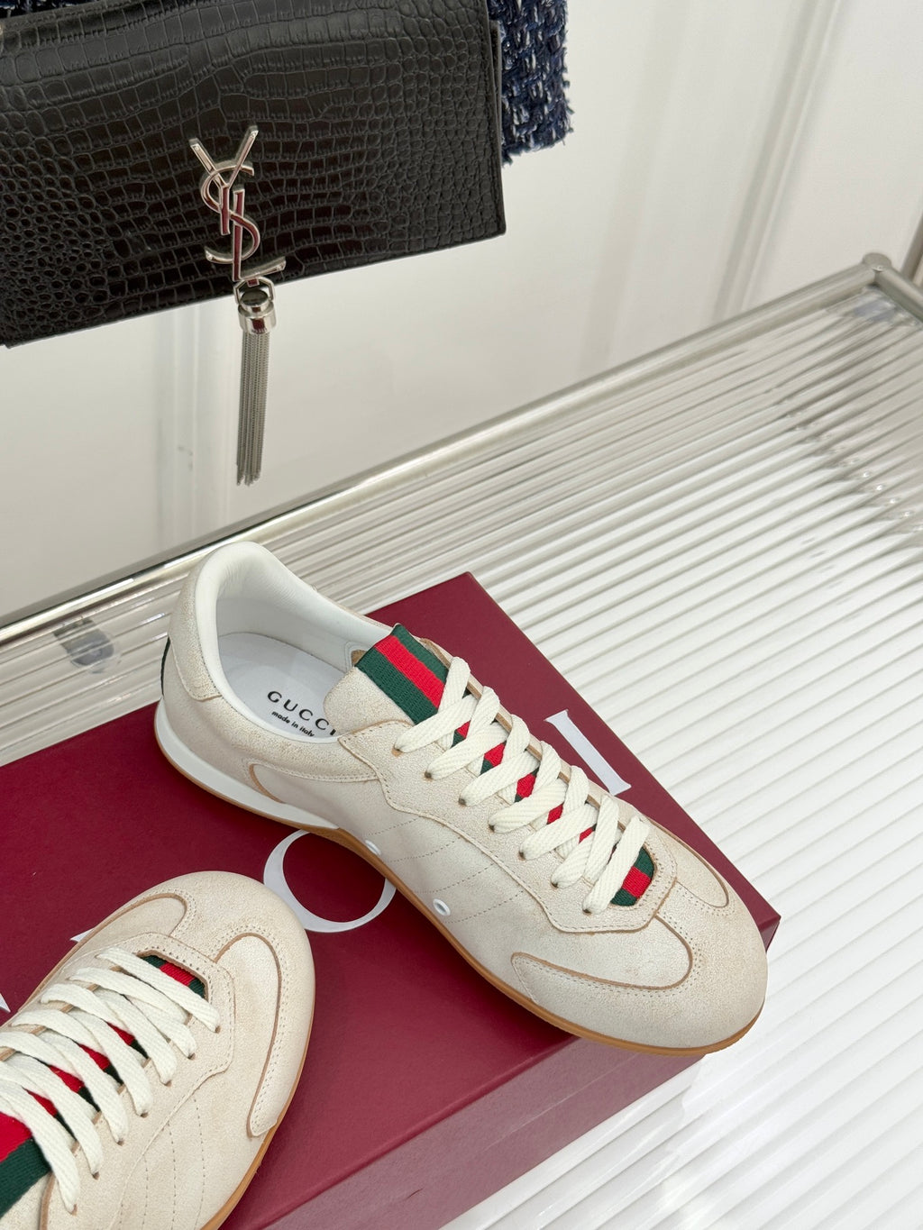 Cream sneakers with green-red web stripe laces, on maroon shoebox