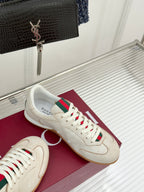 Cream sneakers with green-red web stripe laces, on maroon shoebox