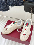Pair of cream sneakers with white laces, green-red web detail, gum outsole