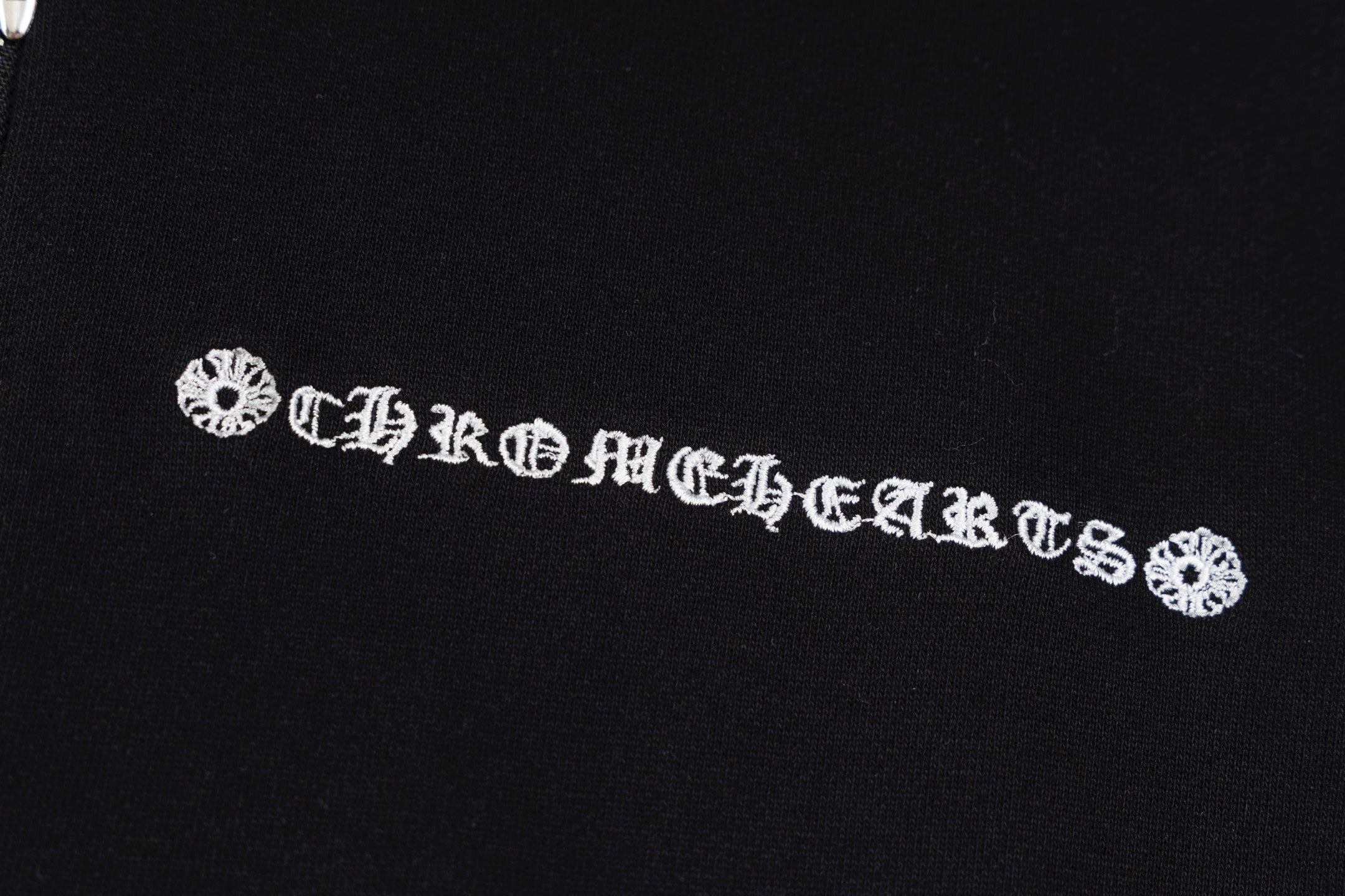 Black hoodie chest emblem with decorative lettering and small floral accents