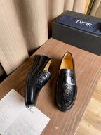 Black leather loafers with embossed detailing and side stitching, shown with one shoe out