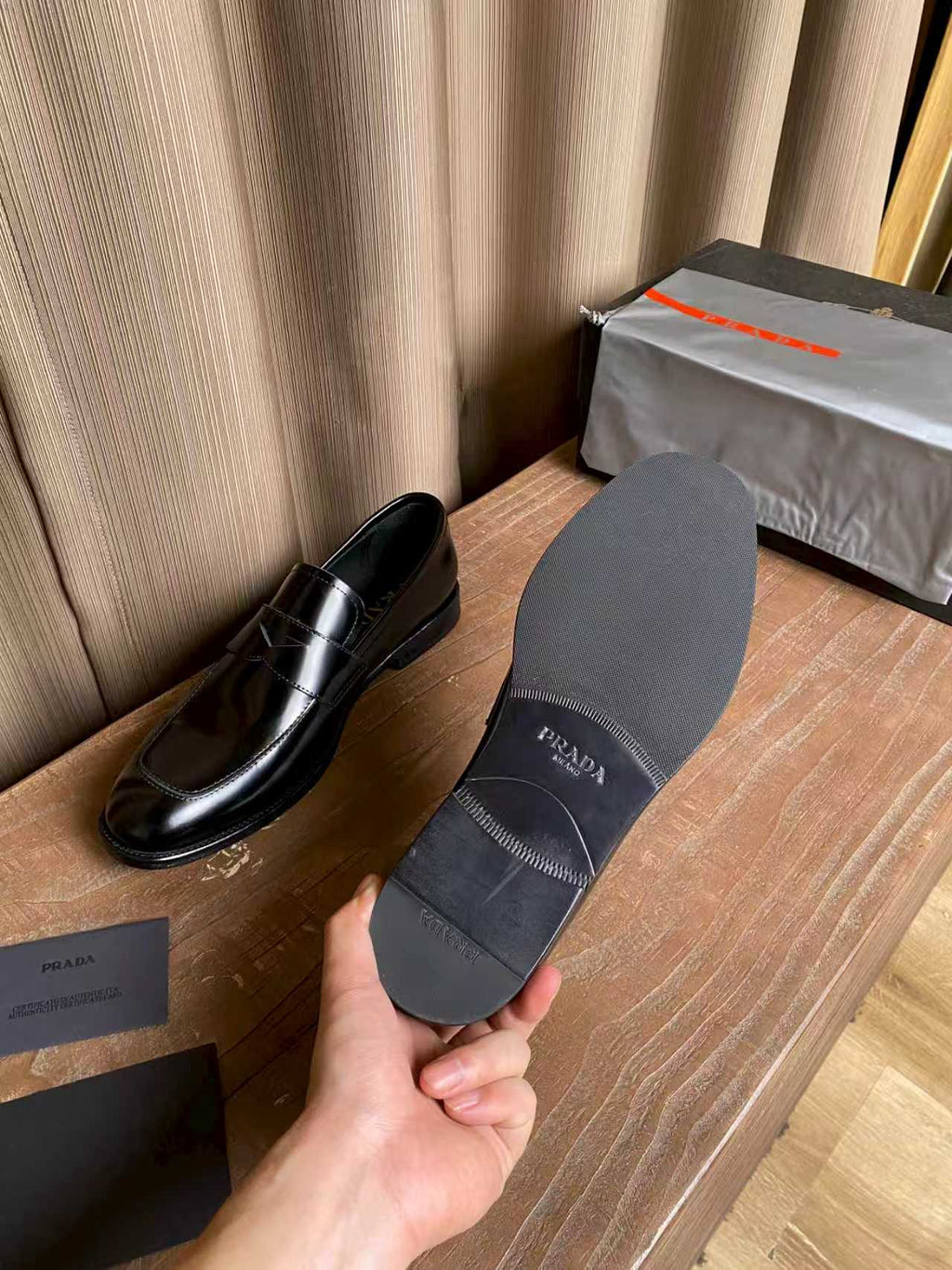 Prada unisex leather loafers and gray dust cover, shown with brand text on cover