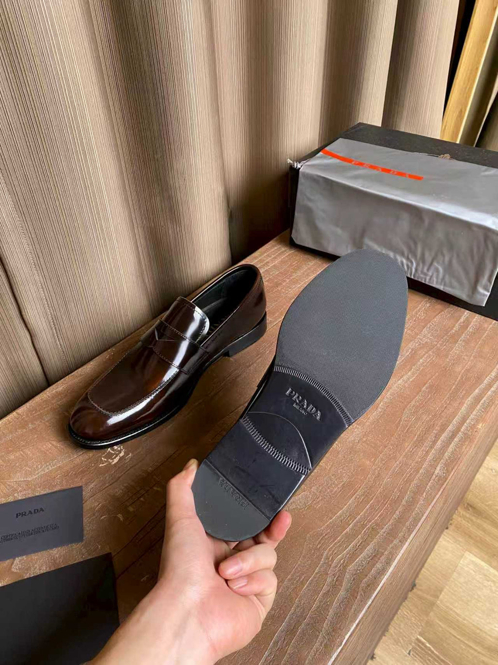 Brown patent leather loafers next to a gray Prada dust bag, slip-on