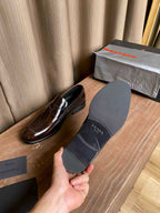 Brown patent leather loafers next to a gray Prada dust bag, slip-on
