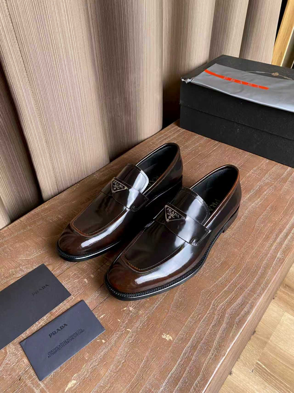 Prada unisex leather loafers, dark brown pair shown from side with metal logo