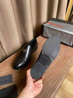 Prada black leather loafers, one shoe held up with strap and logo badge
