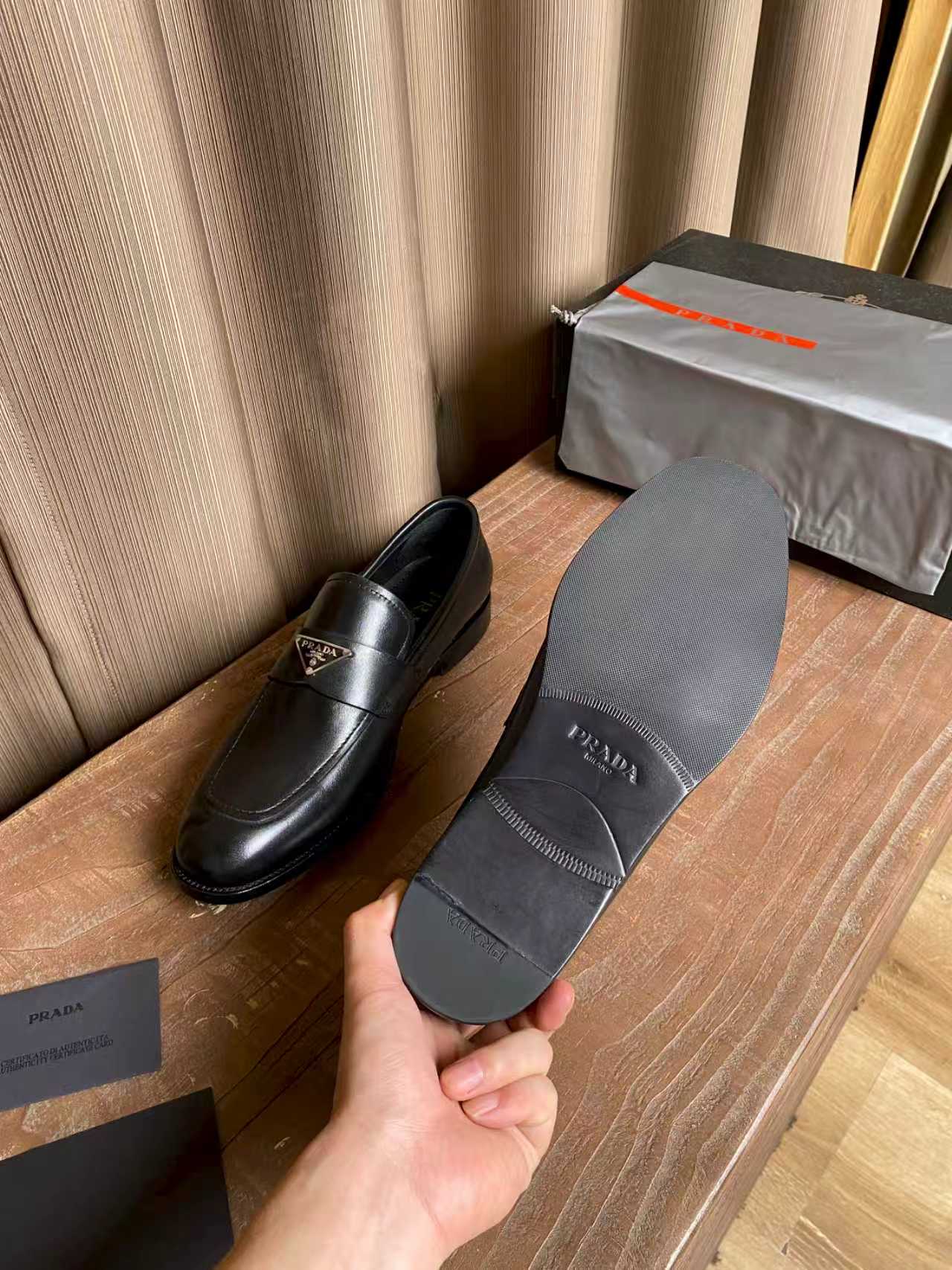 Prada black leather loafers, one shoe held up with strap and logo badge