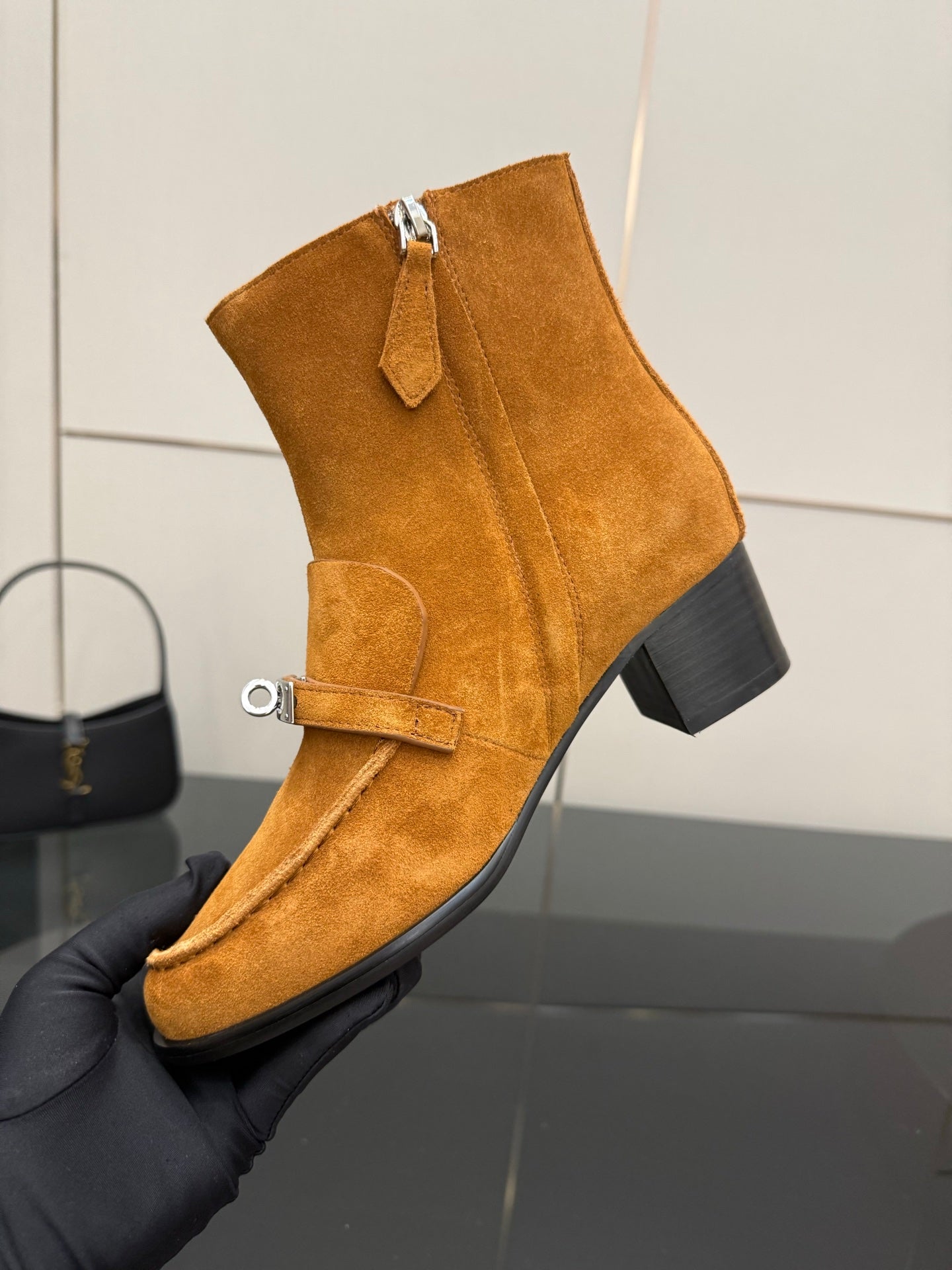 Tan suede ankle boot with zipper and buckle strap, angled close-up.