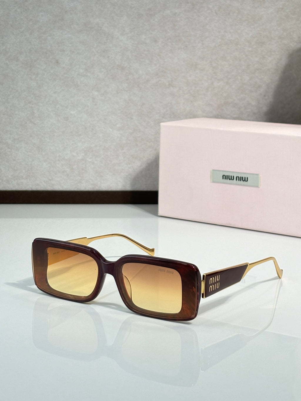 MiuMiu sunglasses with dark brown square frames and gold-toned metal arms