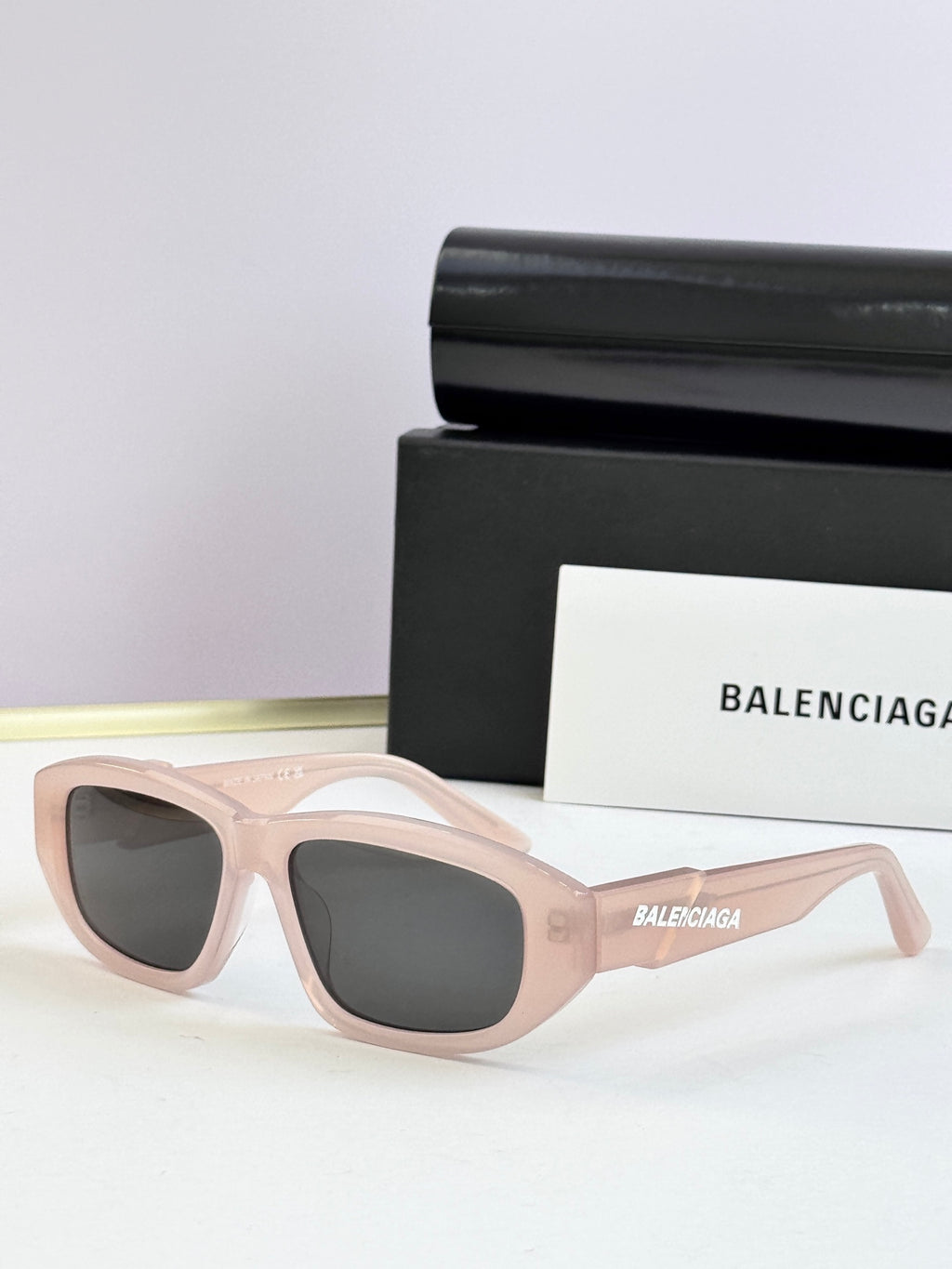 Light pink sunglasses with dark lenses and Balenciaga logo on temple arms