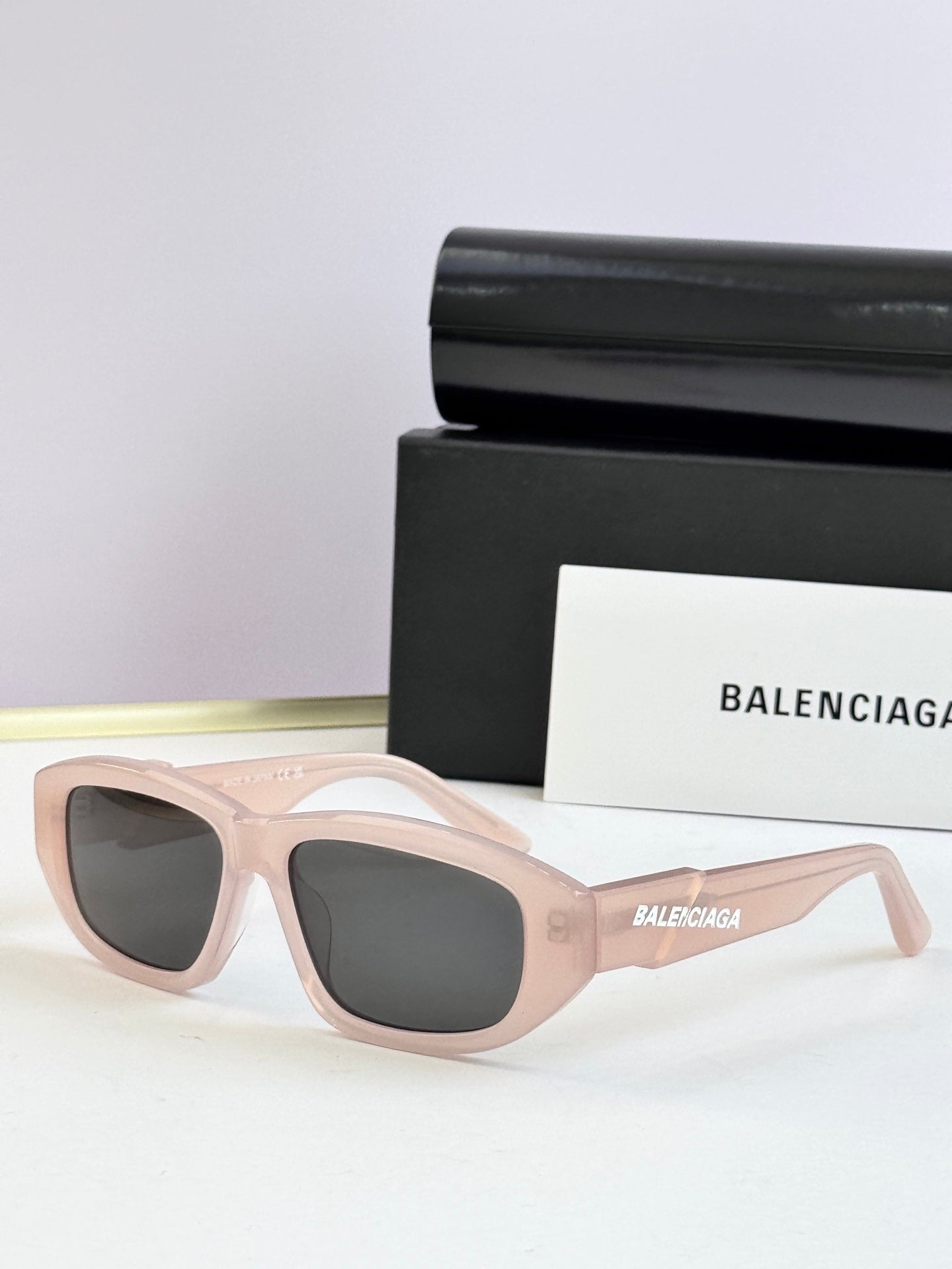 Light pink sunglasses with dark lenses and Balenciaga logo on temple arms