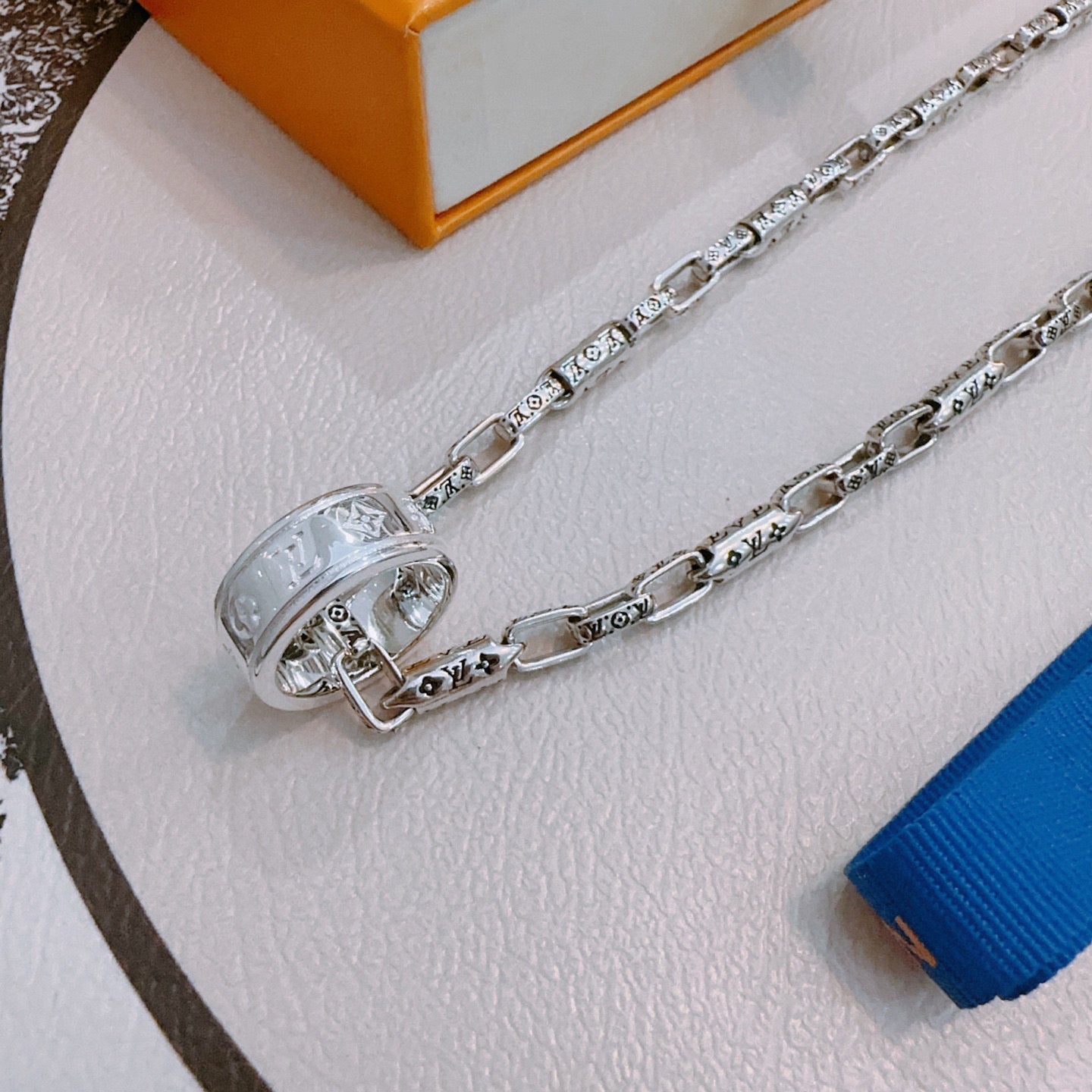 Close-up of silver chain necklace with round clasp and engraved charm