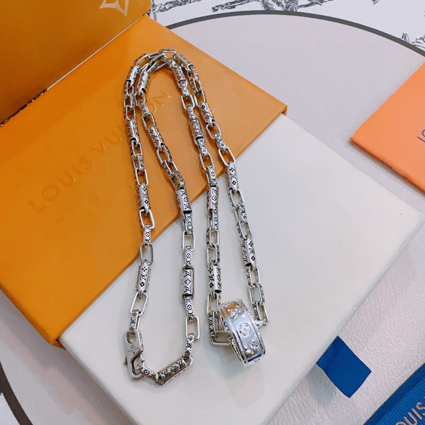 Silver chain necklace with rectangular pendant and lobster clasp, laid on box