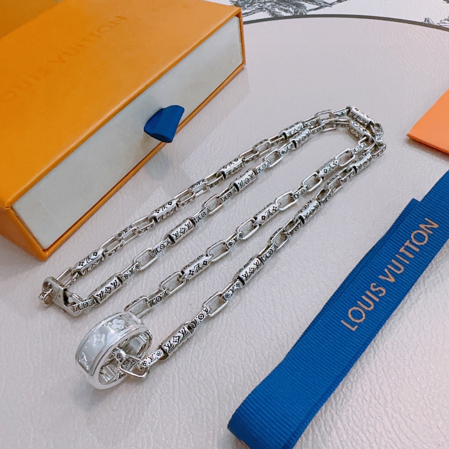 Silver chain necklace with charm clasp and engraved links, draped across display