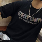 Black graphic T-shirt with silver chain necklace and round pendant at neckline