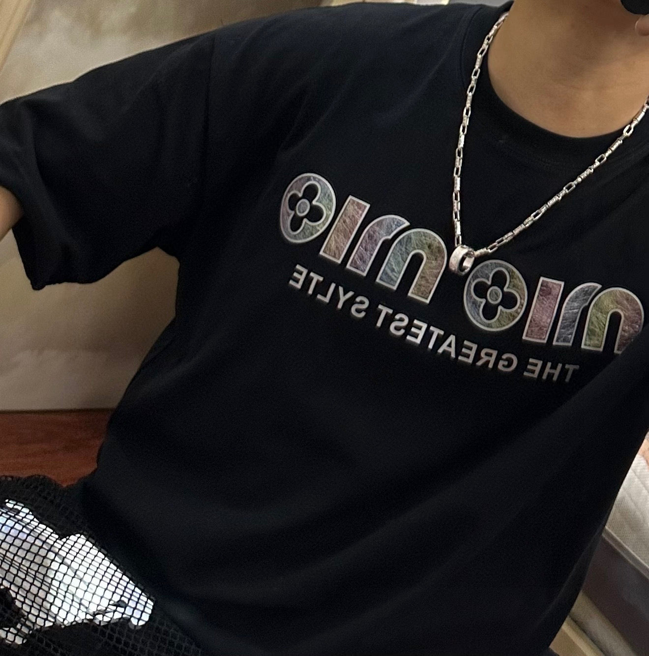Black graphic T-shirt with silver chain necklace and round pendant at neckline