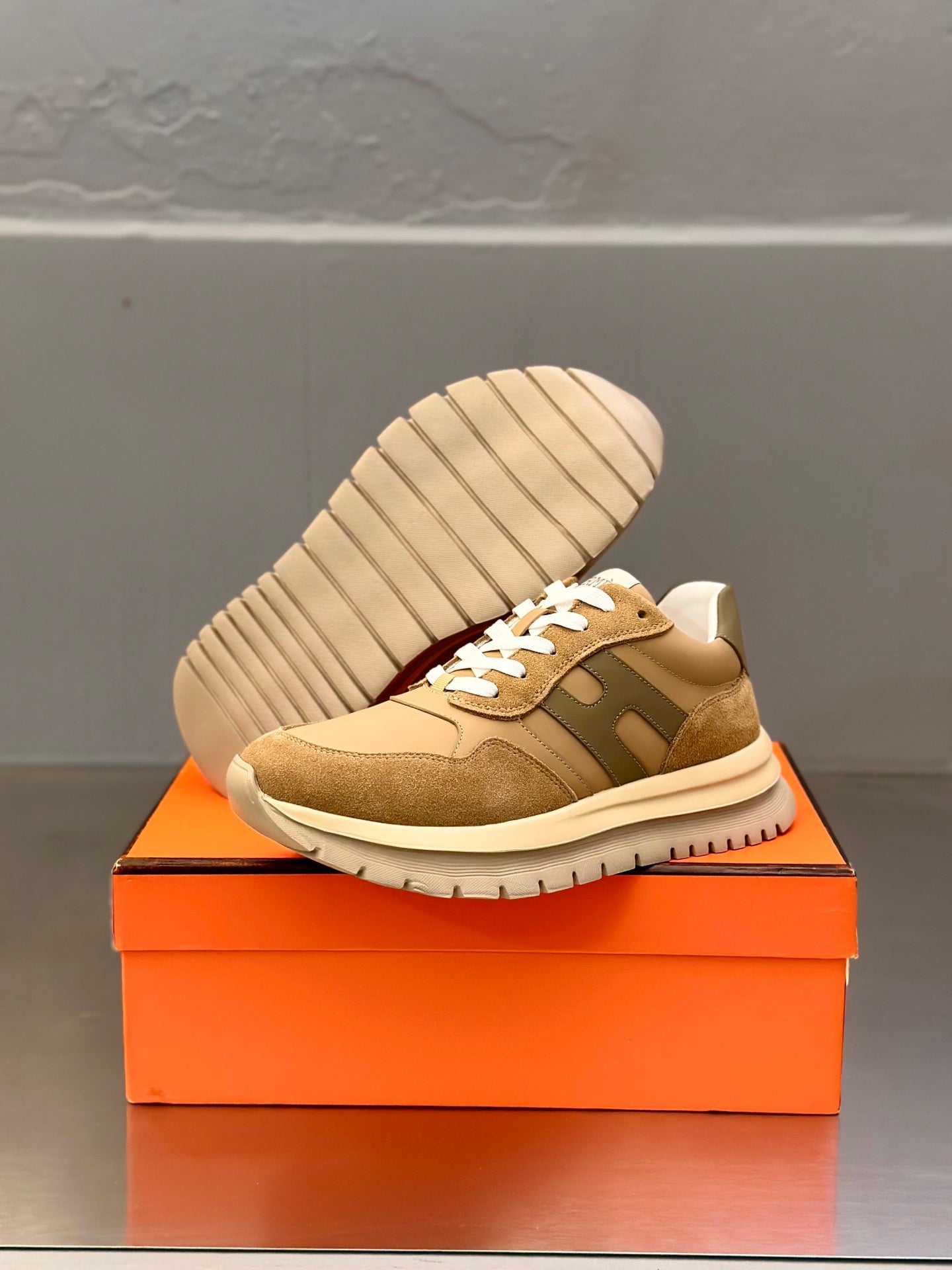 Tan lace-up sneakers with white laces, outsole visible on orange box