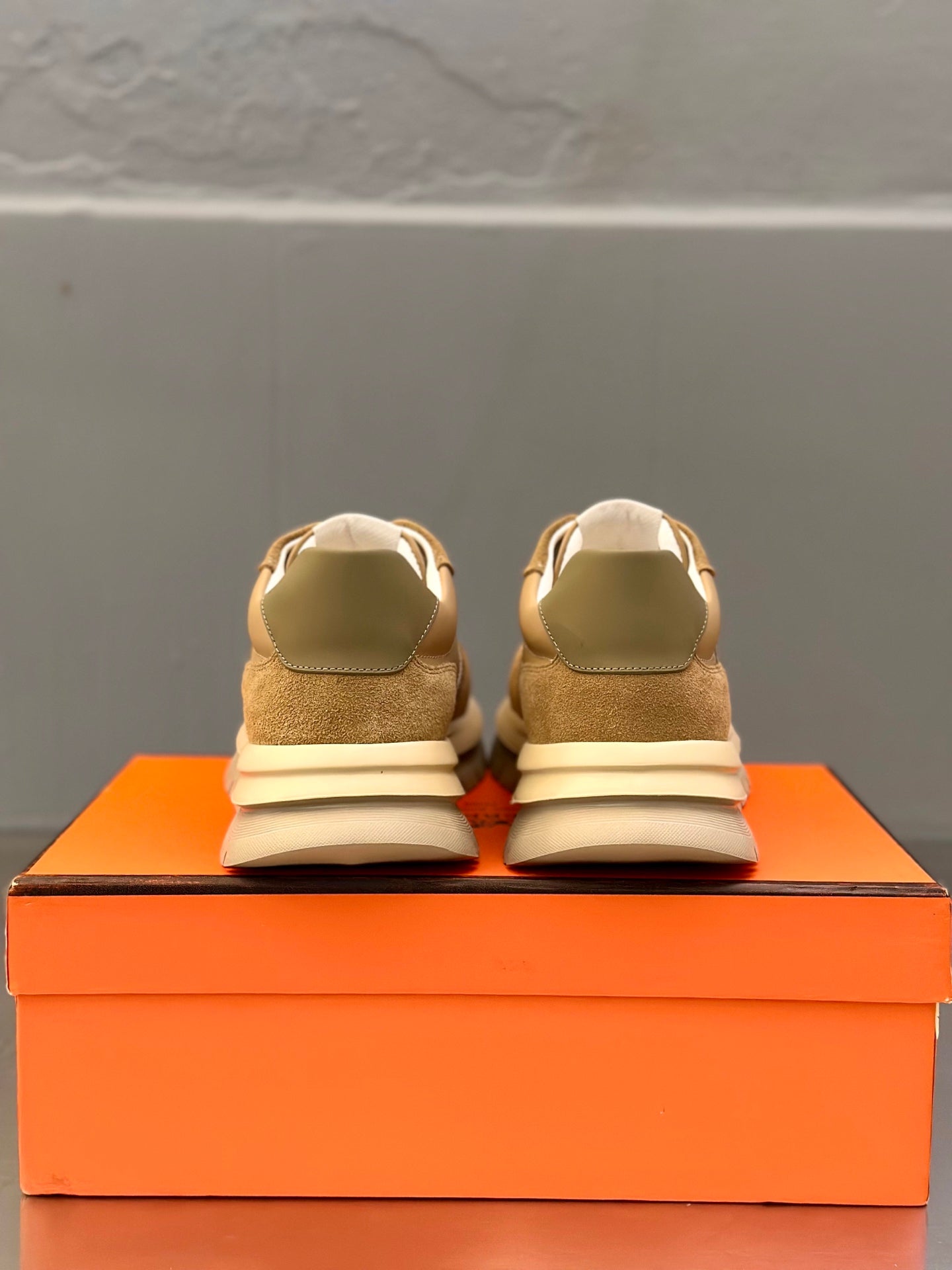 Back view of tan lace-up sneakers with white laces, on orange box
