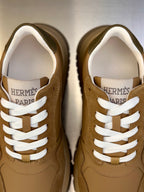 Close-up of tan lace-up sneakers with white laces and HERMES PARIS on tongue