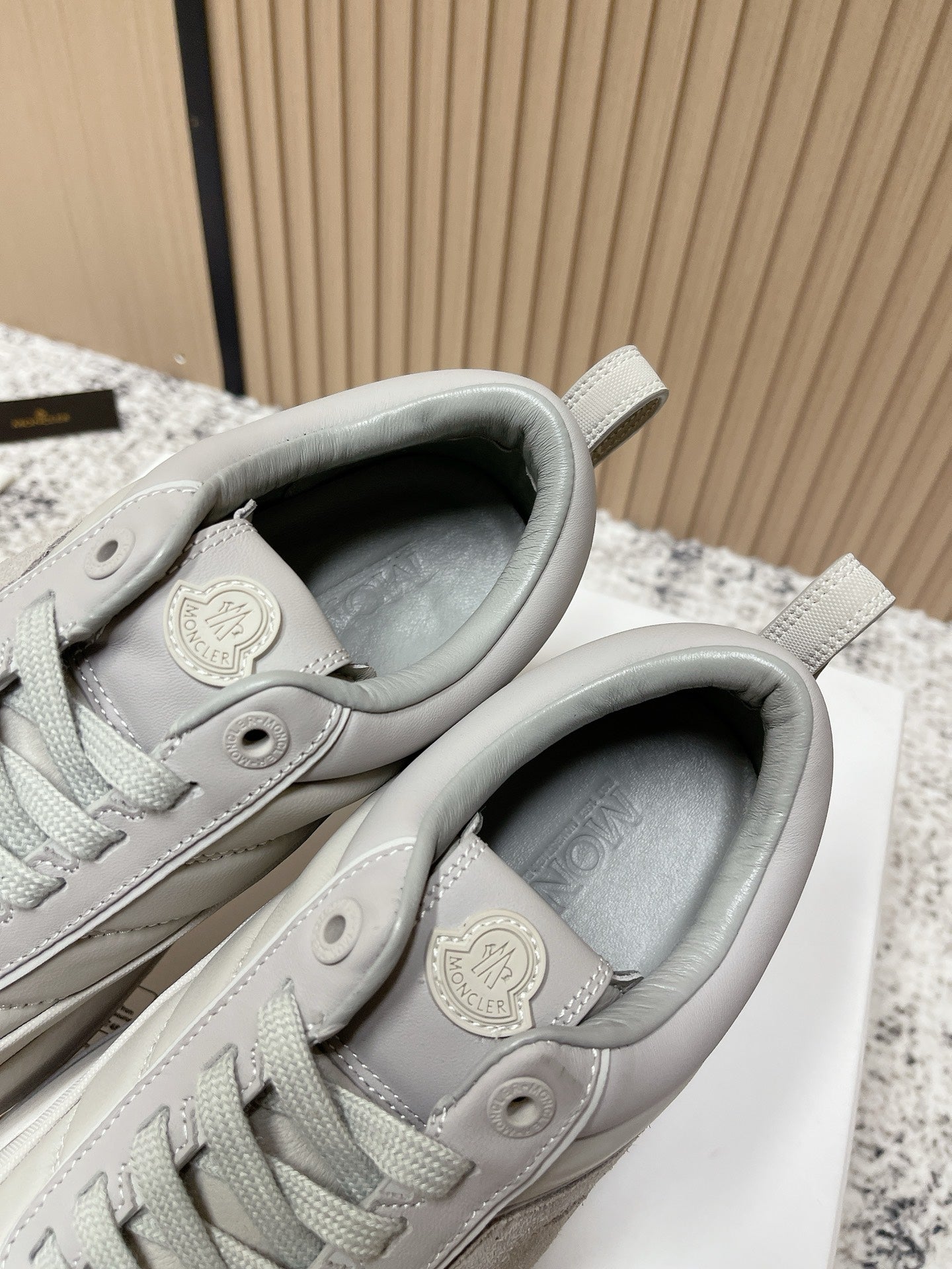 Light gray sneakers with padded collar and circular Moncler patch at heel