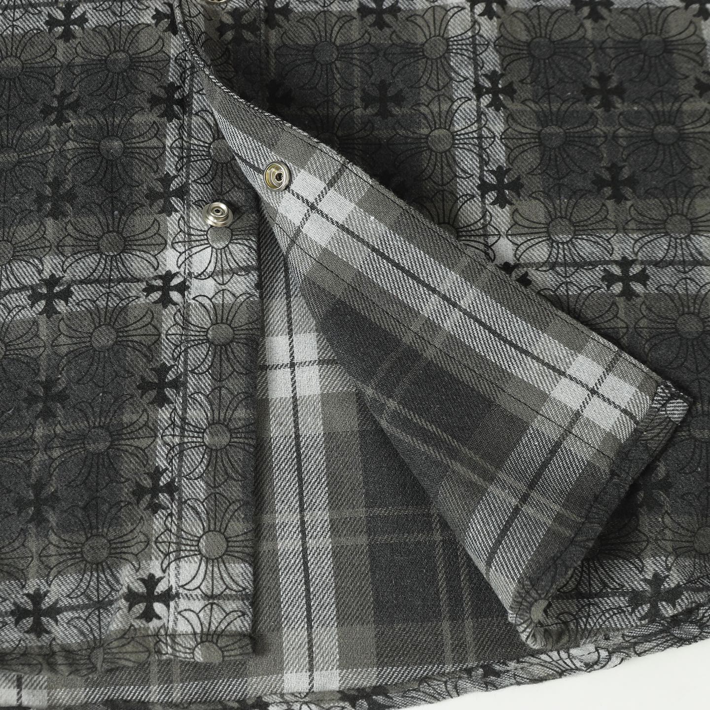 Dark gray button-up shirt sleeve with plaid inner facing and gold buttons