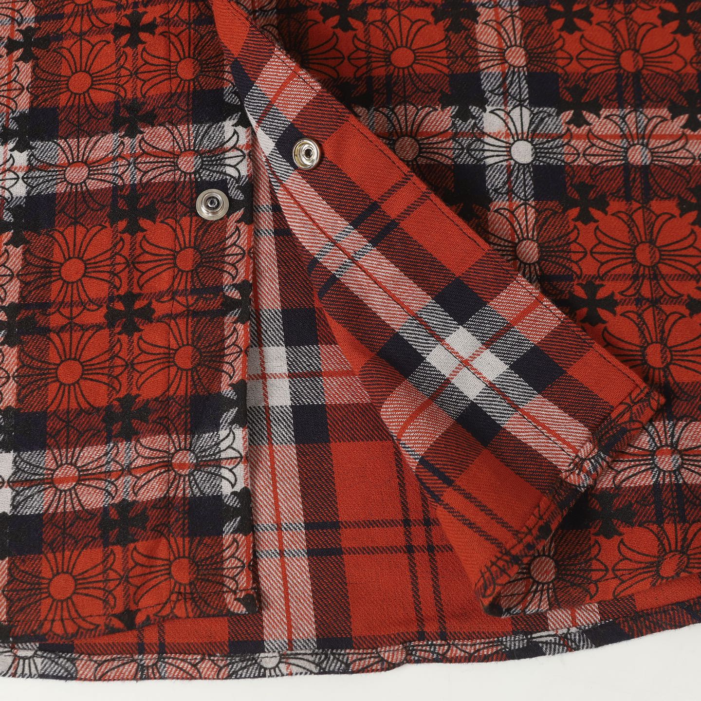 Long-sleeve shirt sleeve detail with red and white plaid and a silver snap button