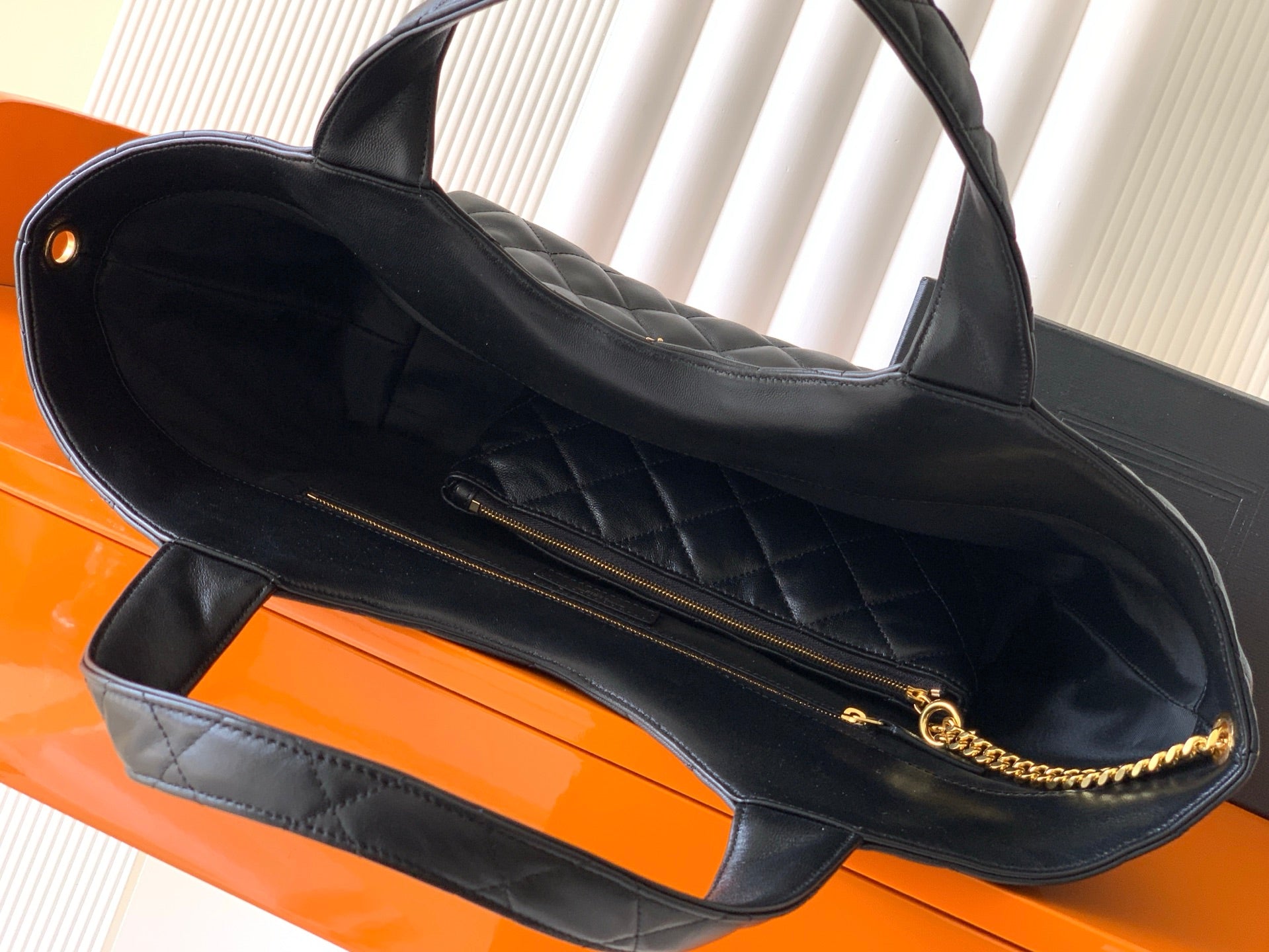 Black quilted tote bag interior view with zip pocket and gold chain