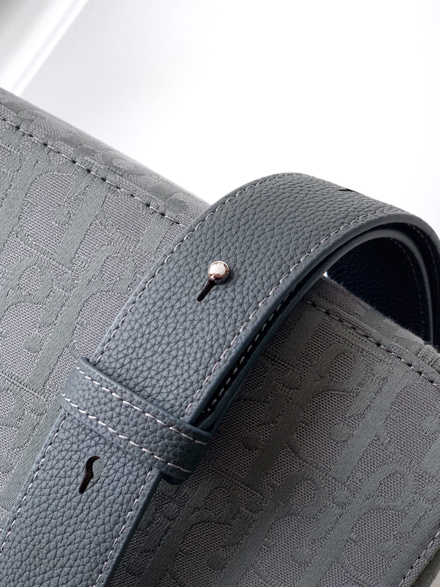 Close-up of crossbody bag side flap seam, dark gray textured leather and logo