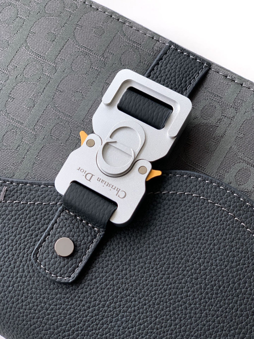 Close-up of crossbody bag strap buckle, dark gray logo fabric and leather patch