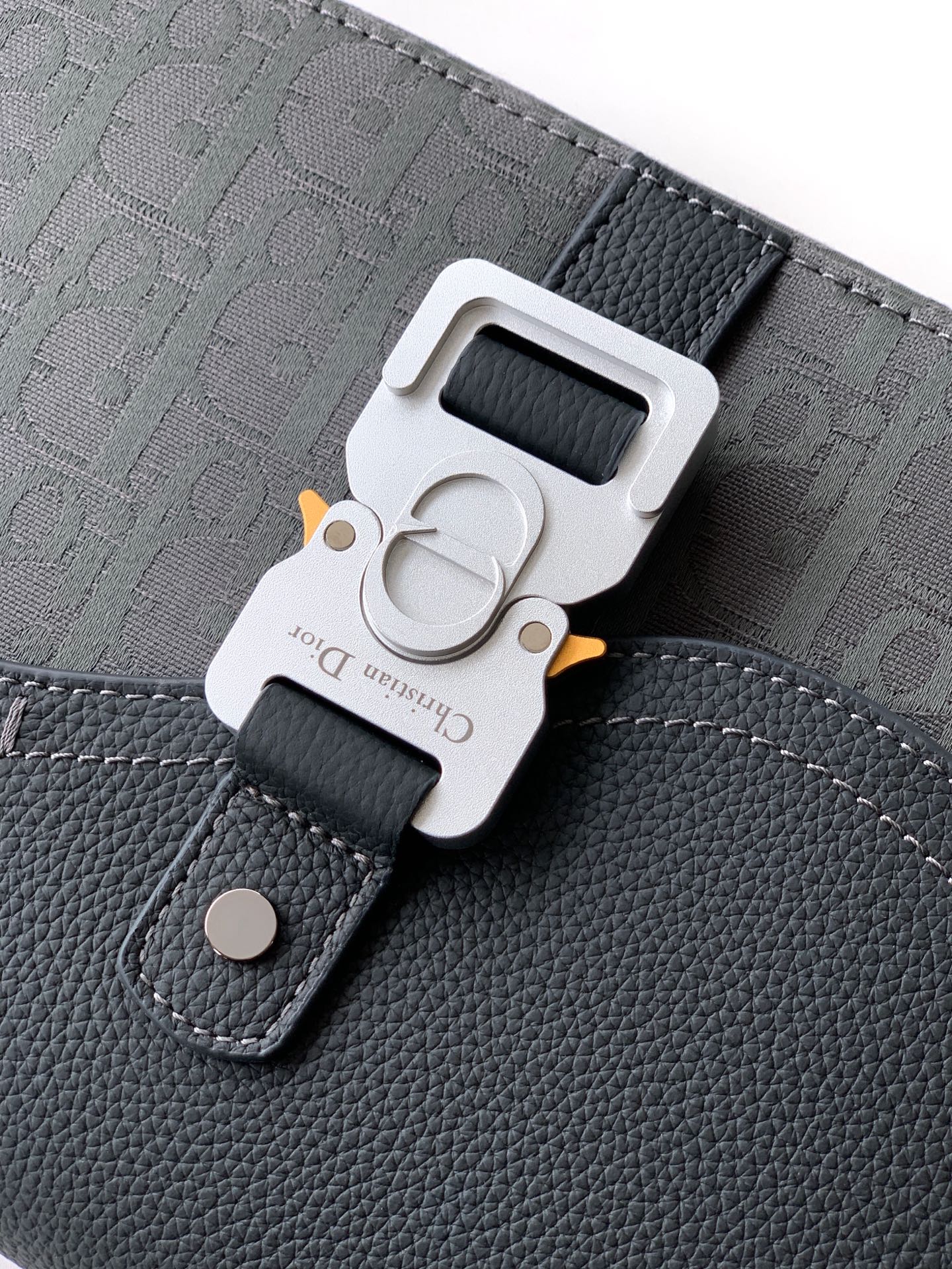 Close-up of crossbody bag strap buckle, dark gray logo fabric and leather patch