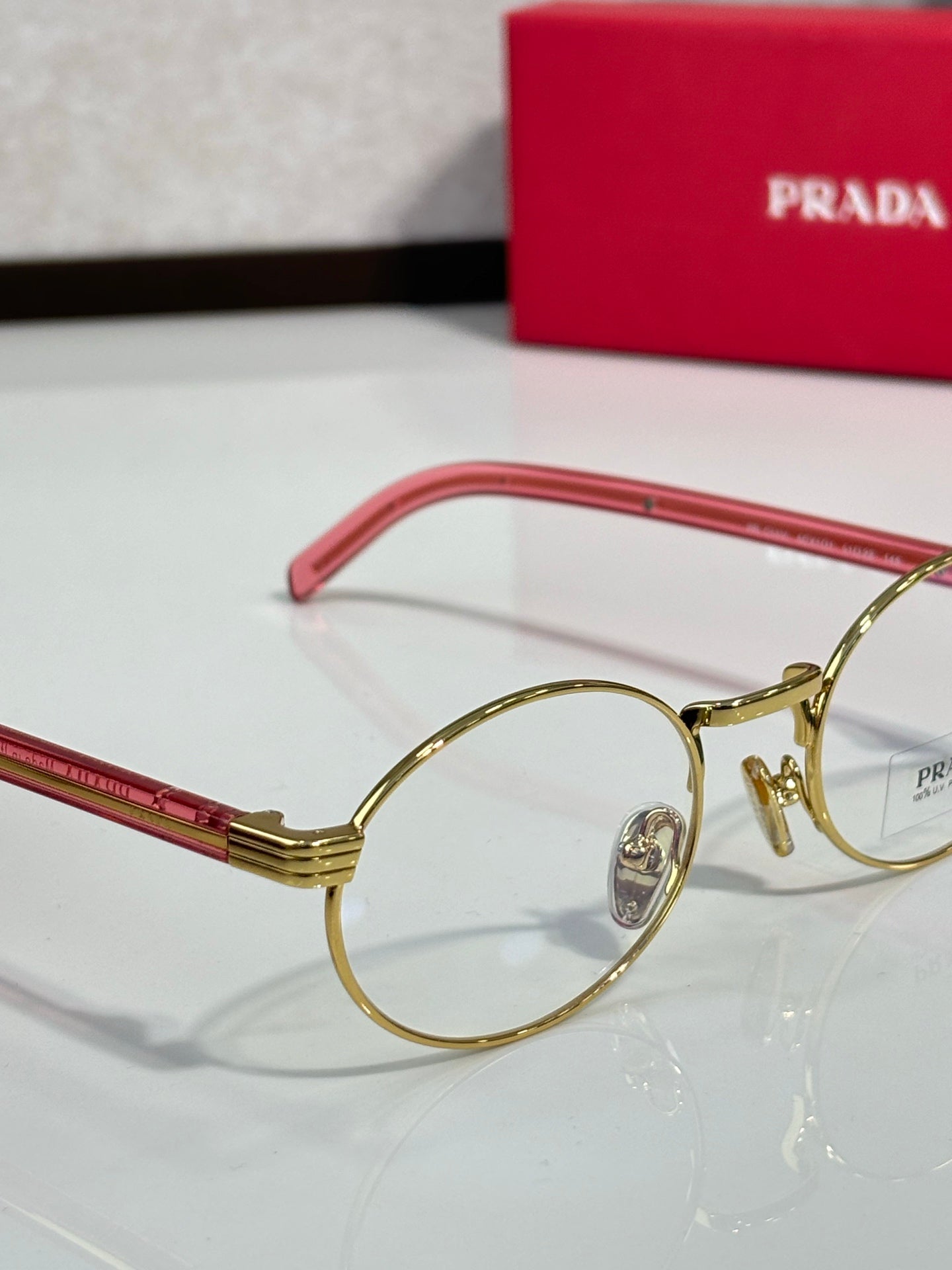 Round eyeglasses close-up with red-pink temple, gold frame and clear lens