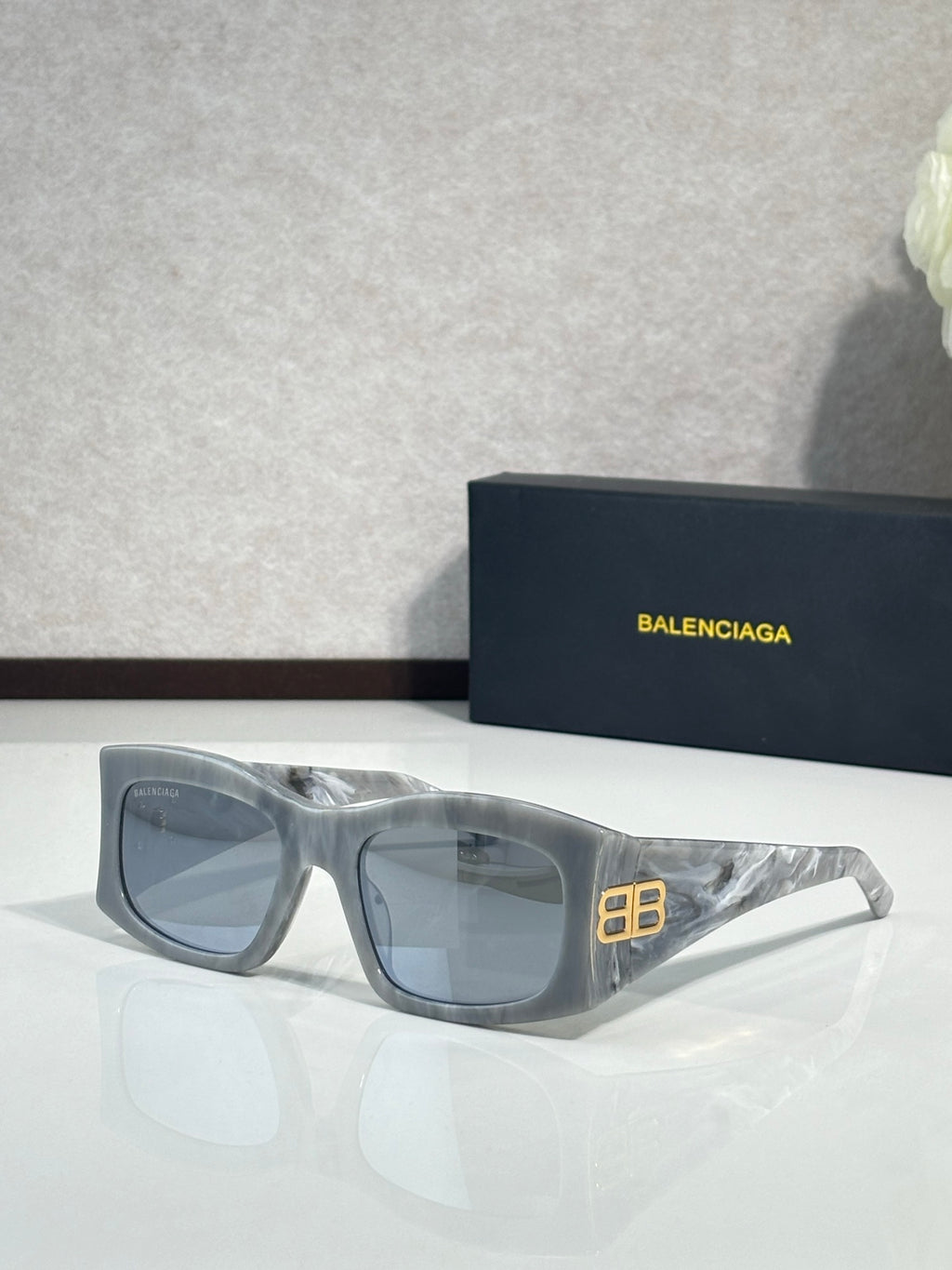 Balenciaga sunglasses with blue-tinted lenses and light gray acetate frame, gold logo