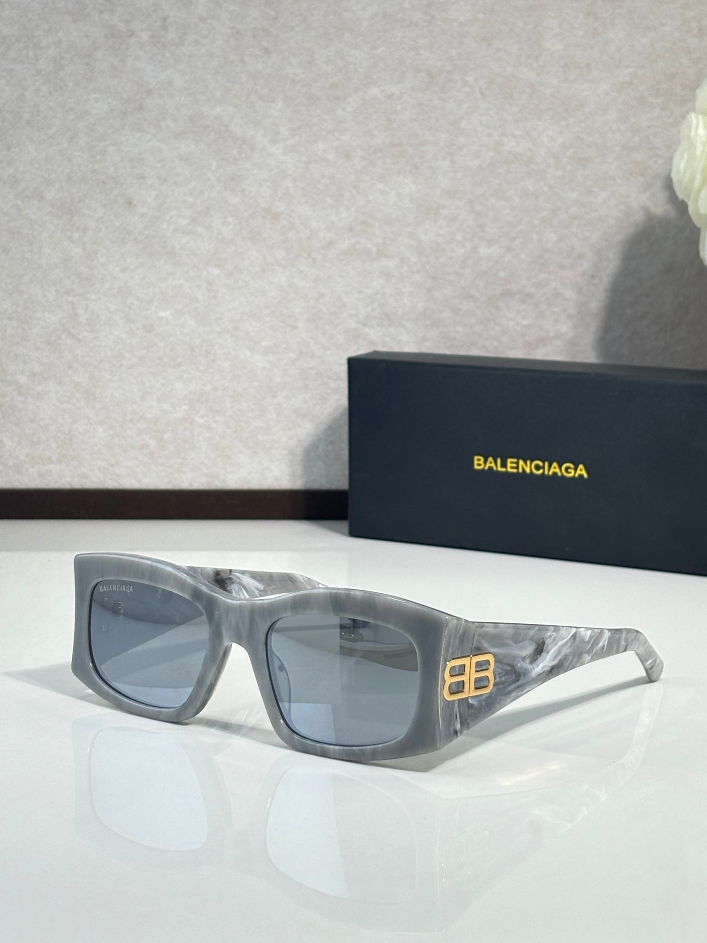 Balenciaga sunglasses with blue-tinted lenses and light gray acetate frame, gold logo