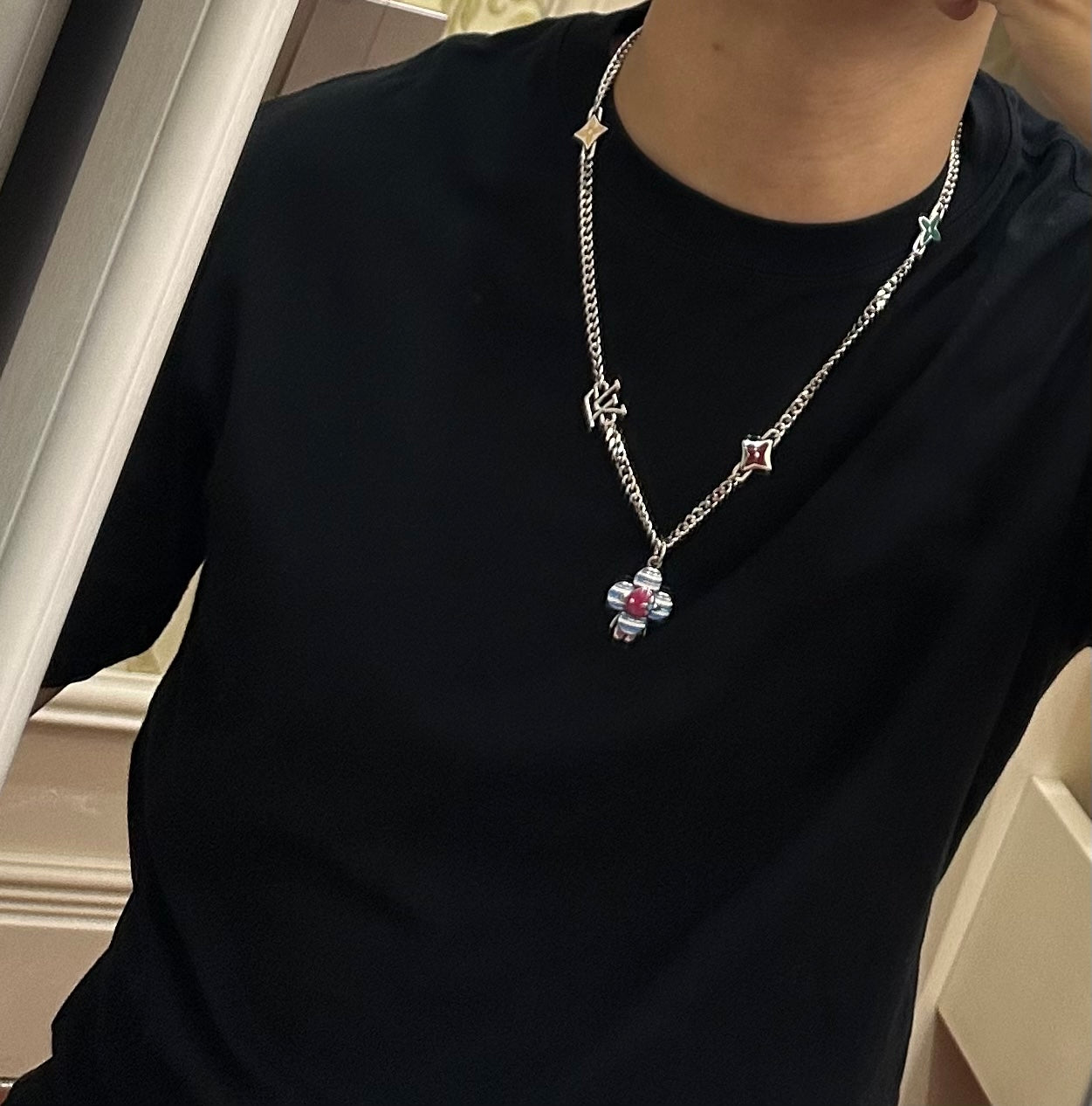 Silver charm necklace worn on black shirt; multicolor flower drop pendant at center