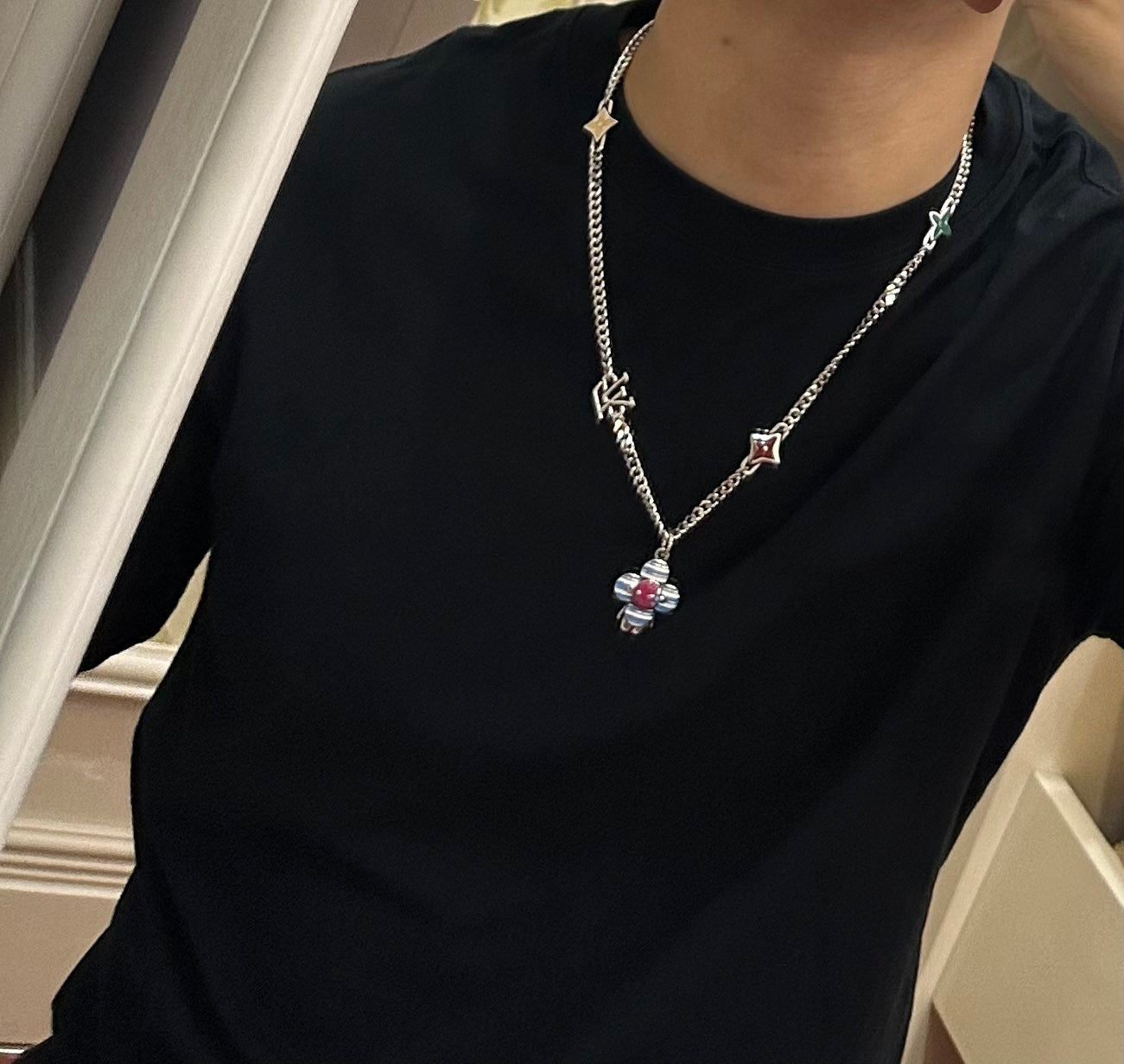 Silver charm necklace worn on black shirt; multicolor flower drop pendant