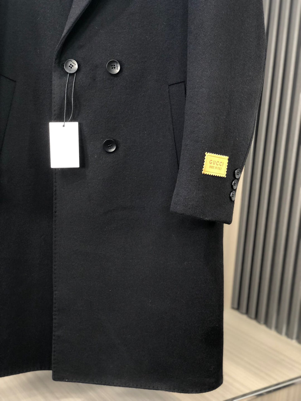 Black long coat close-up with button details and small Gucci patch on sleeve