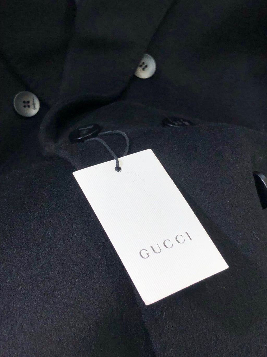 Dark coat with white GUCCI-branded hang tag near button placket