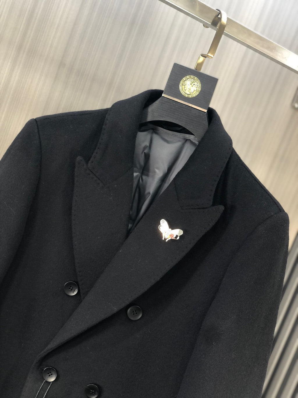 Black coat lapel with embroidered butterfly pin detail and dark button front
