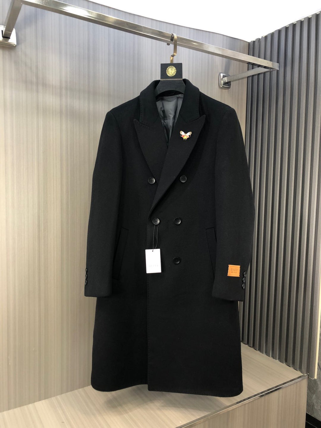 Black long double-breasted coat with notch lapels and button front, with small butterfly pin