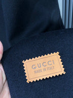 Clothing tag reading GUCCI MADE IN ITALY attached to dark coat