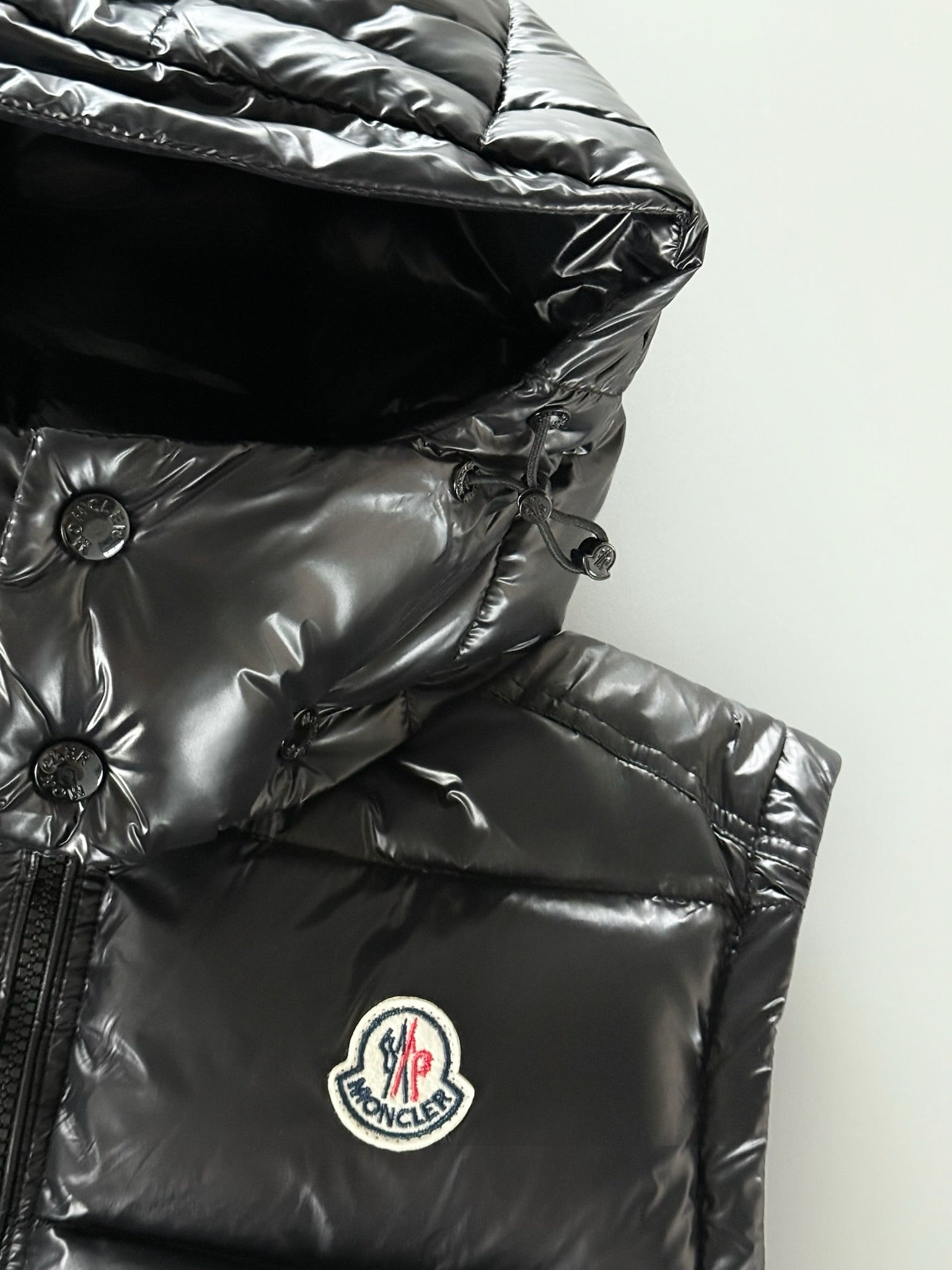 Black Moncler hooded puffer jacket with oval chest logo patch on quilted fabric.
