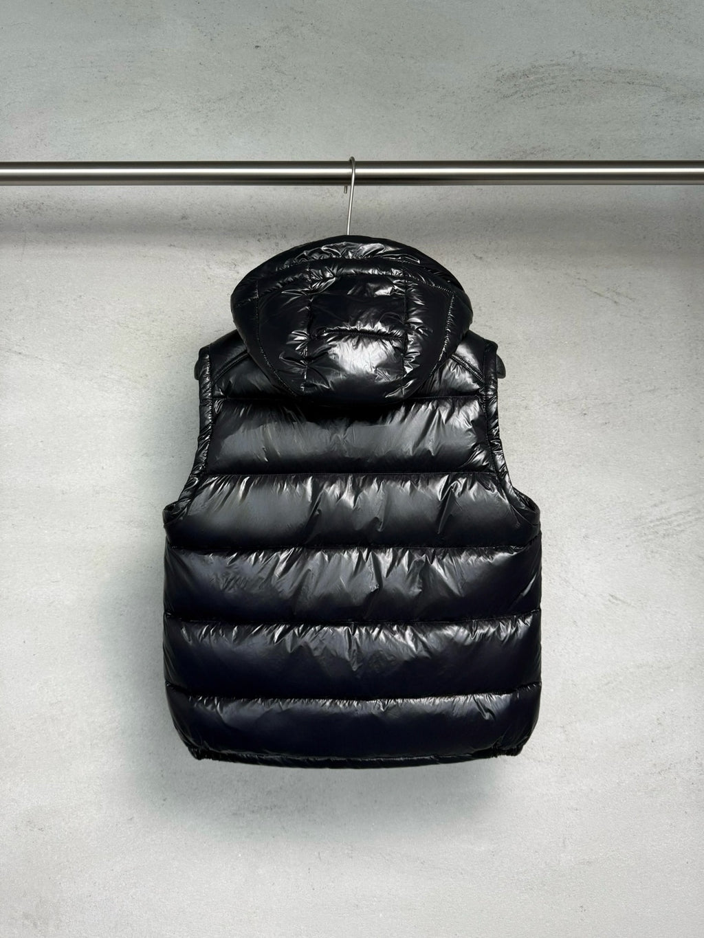 Black hooded puffer vest with quilted panels, front zipper, and chest logo detail.