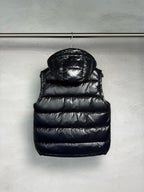 Black hooded puffer vest with quilted panels, front zipper, and chest logo detail.