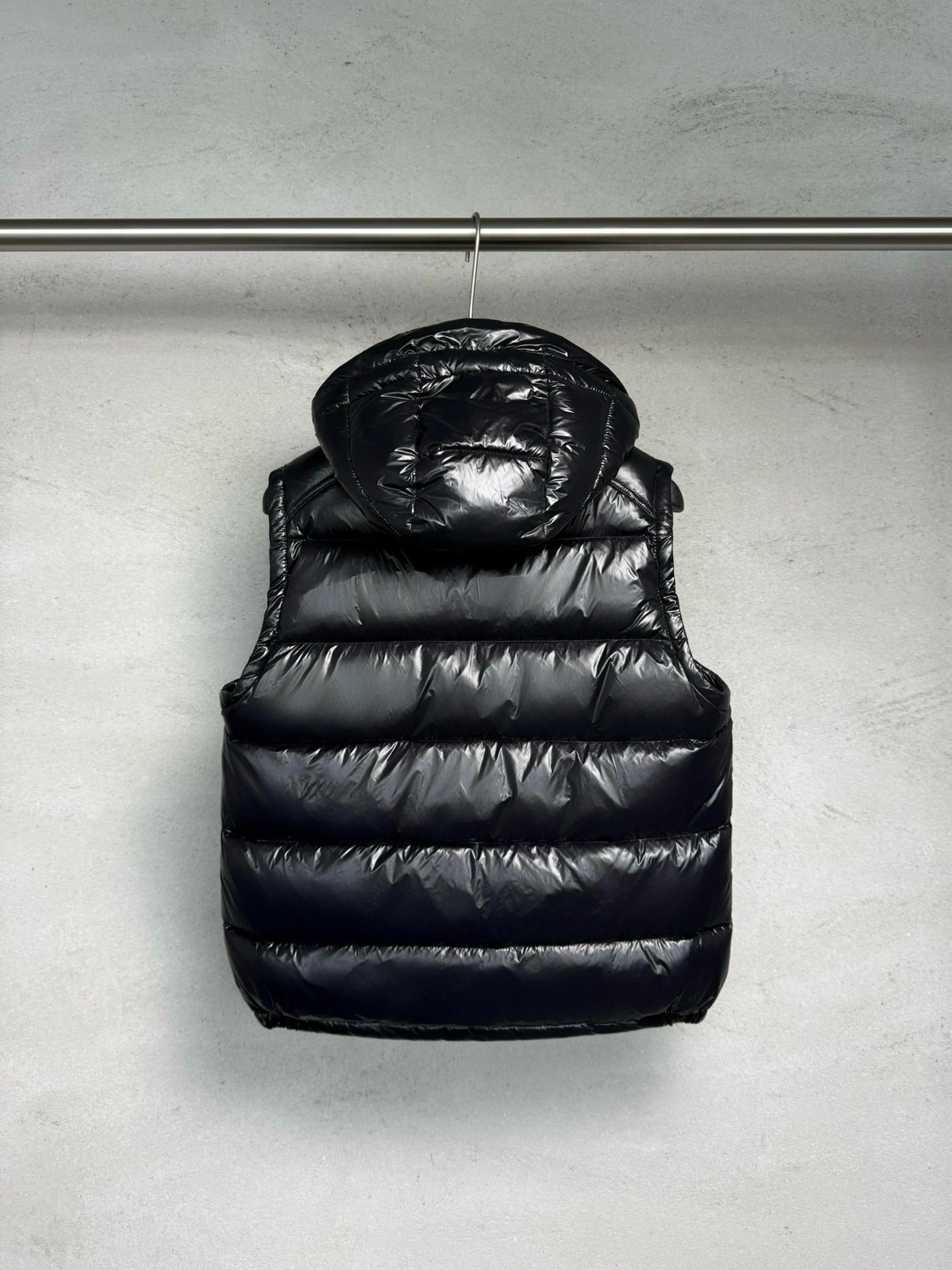 Black hooded puffer vest with quilted panels, front zipper, and chest logo detail.