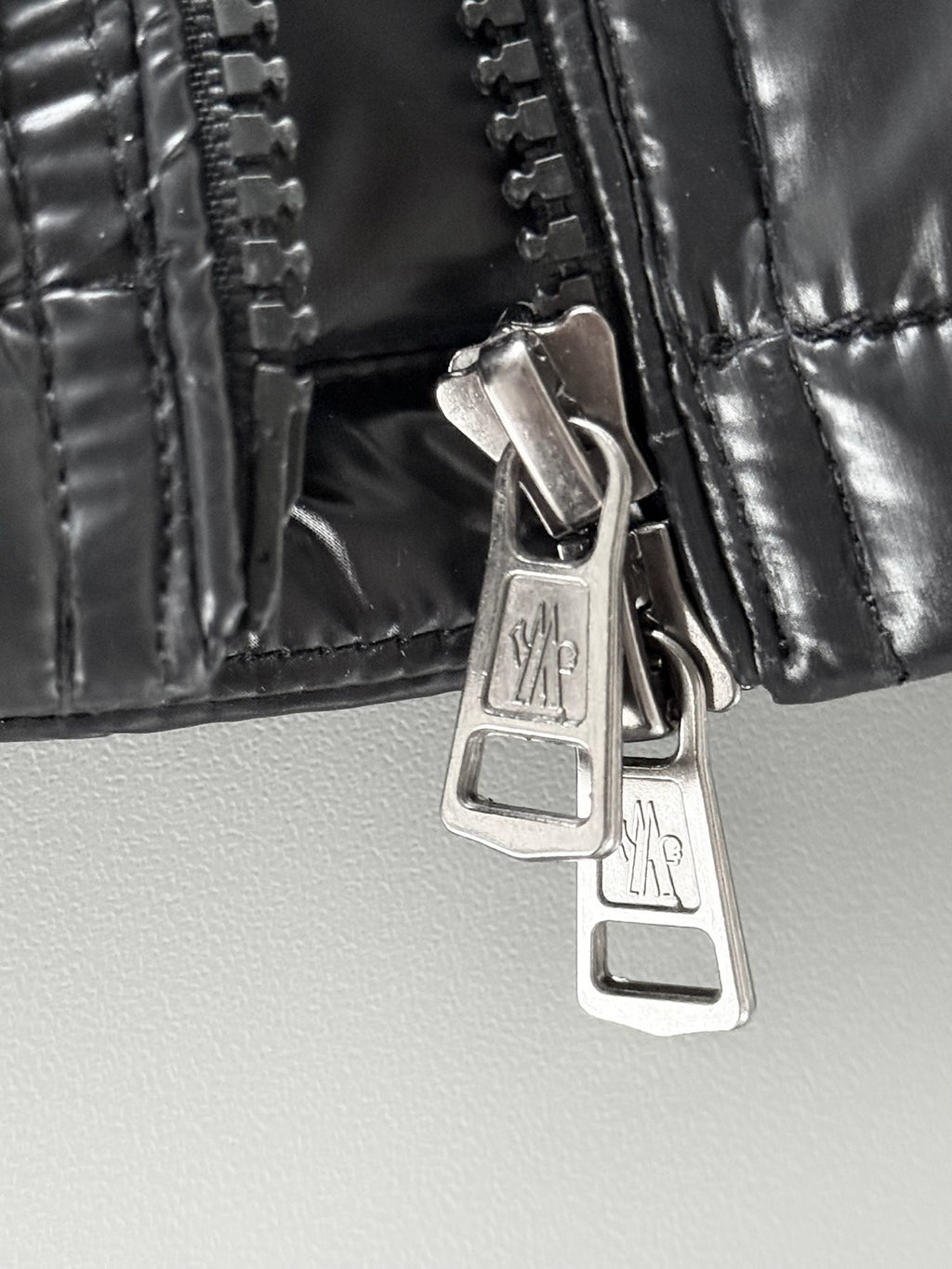Black puffer jacket close-up of zip placket with metal zipper pulls.