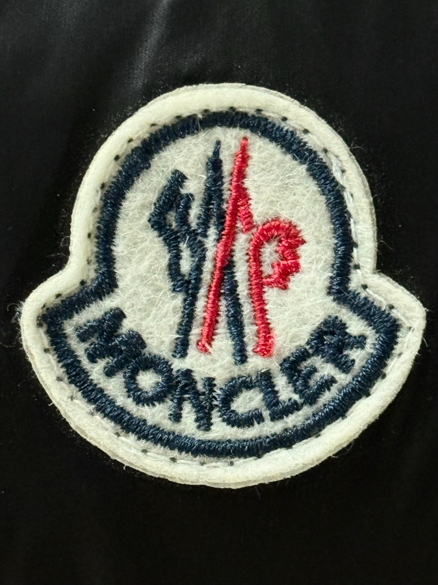 Embroidered Moncler logo patch in red and blue on black fabric.