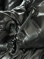Black puffer fabric close-up with metal snaps, zipper pulls, and small circular logo.