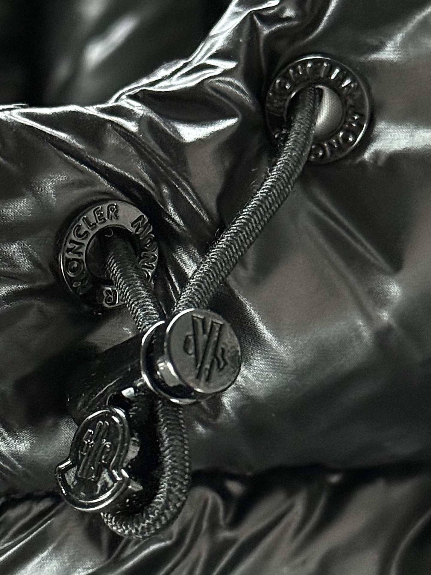 Black puffer fabric close-up with metal snaps, zipper pulls, and small circular logo.