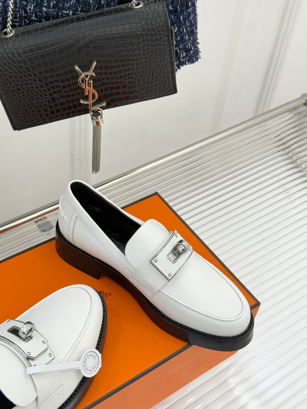 Hermes white leather loafer side view with silver buckle detail and black rubber sole