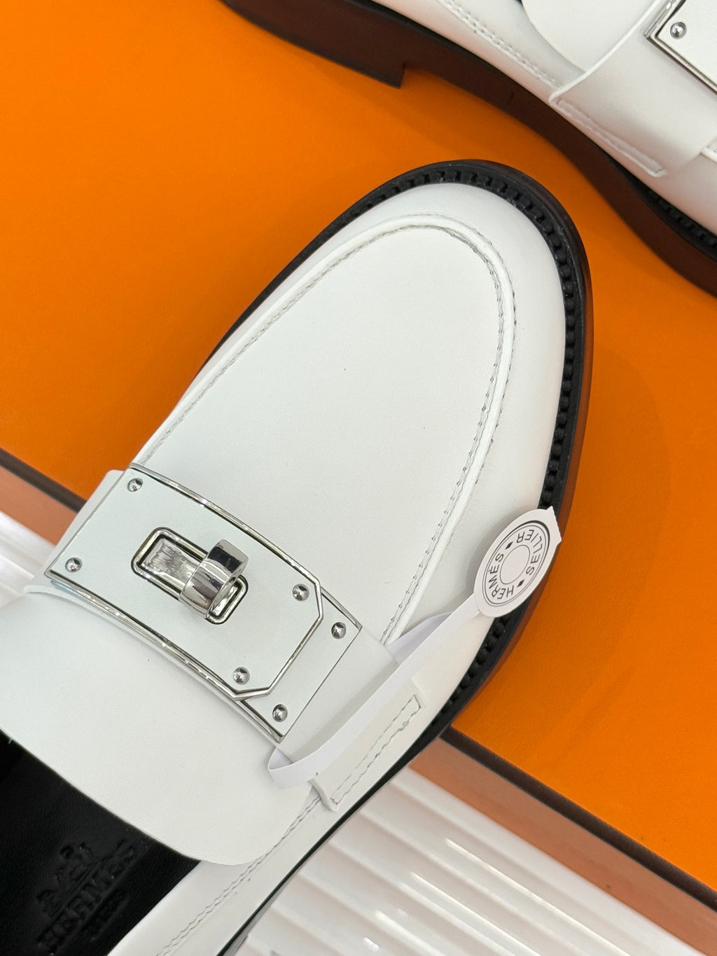 Hermes white leather loafer close-up with silver buckle bar and round emblem